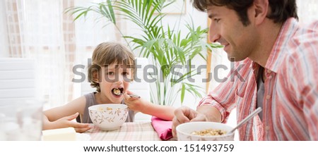 Panoramic view of a single parent dad and his young son having breakfast together and eating cereals during a sunny morning at home, interior.