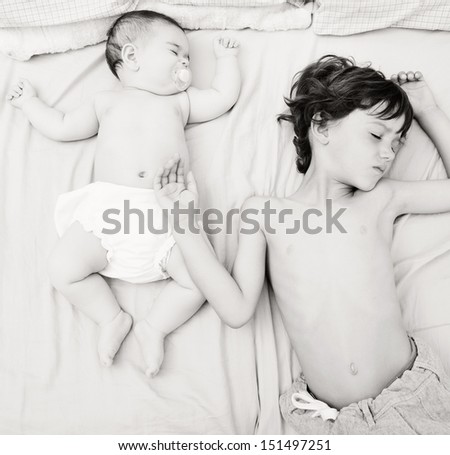 Over head view of a boy child and a baby girl sleeping together and sharing a bed, in the same body position.