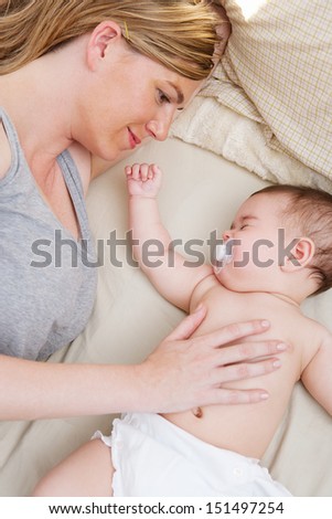 Close up portrait over head view of a mother and her baby daughter relaxing on a bed at home, with the infant sleeping and mom caring for her.