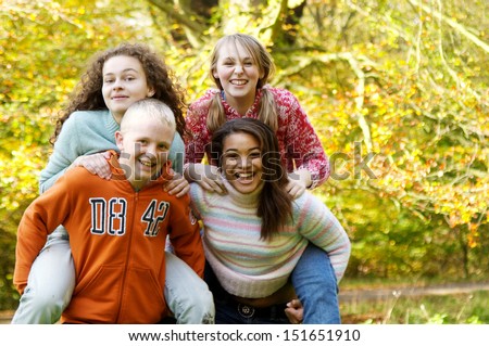 Four young teenager friends playing piggy bag racing game in a park forest during the fall autumn season with yellow trees, having fun, laughing and running together.