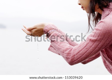 Close up side portrait of an asian young woman holding her hands together while standing on a lake with pure and clean water filtering through her fingers.