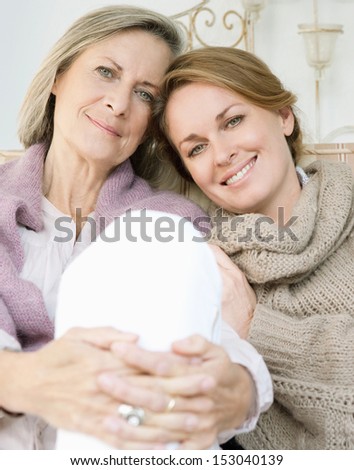 Close Up Family Portrait Of An Adult Daughter With Her Mature Mother Leaning On Each Other And Being Affectionate While Relaxing On A Sofa At Home, Outdoors.