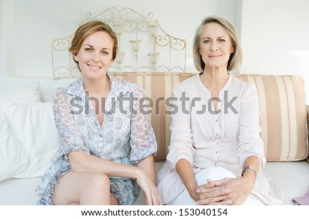 Family portrait of an adult daughter and her mature mother lounging together on a sofa in the garden at home, relaxing and being comfortable.