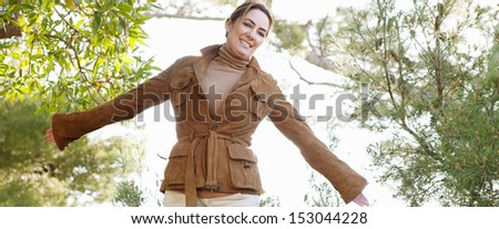 Panoramic view of an attractive middle aged woman visiting the forest countryside during the autumn season, wearing a leather jacket and feeling carefree, smiling with sunshine.