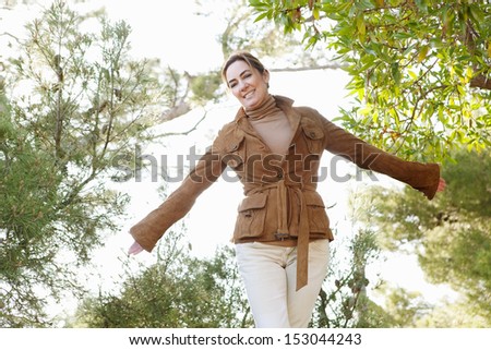 Portrait of an attractive middle aged woman visiting the forest countryside during the autumn season, wearing a leather jacket and feeling carefree, smiling with sunshine.