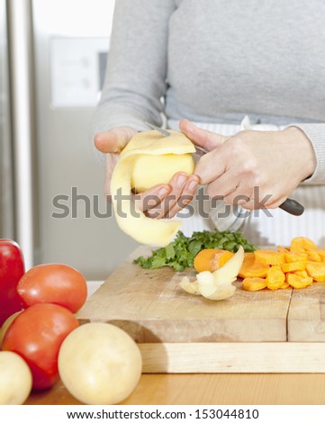 Close up detail of a woman hands pealing potatoes and preparing various vegetables in the kitchen at home using a wooden chopping board, interior.
