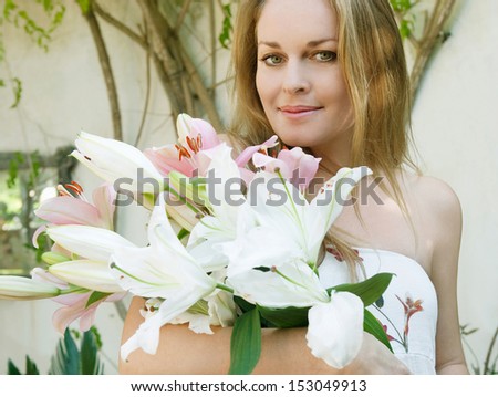 Portrait of an attractive woman holding a bunch of white and pink lilies flowers while relaxing in a home garden during a sunny day, exterior.