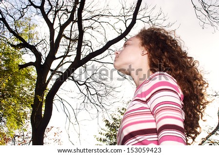 Side portrait view of a young teenager girl standing in an autumn winter forest park with bare trees, contemplating and relaxing while being thoughtful and serene, outdoors.