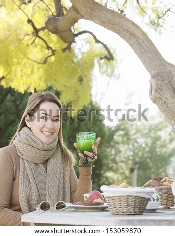 Attractive woman sitting at a table in her home garden having a healthy breakfast during a sunny autumn day, enjoying eating and drinking a glass of orange juice outdoors.