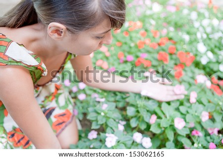 Over head portrait view of an attractive young woman leaning forward to pick a pink flower from a blossom bush in a park during a sunny spring day out, exterior.