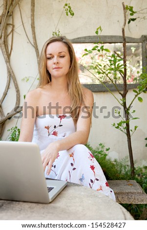 Portrait of a woman relaxing in a garden and using a laptop computer during a sunny day on vacation, enjoying a warm morning outdoors.