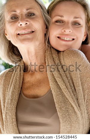 Close up portrait of a mature mother and adult daughter being close and spending time together in a home garden being affectionate and joyful during a bright and golden summer sunny day.