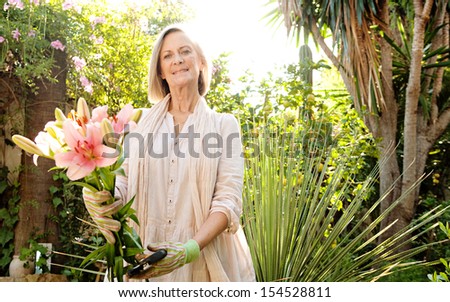 Attractive mature woman holding a bunch of freshly cut japanese lilies flowers during a sunny day in the garden, smiling proud, outdoors.