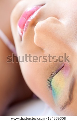 Over head close up beauty portrait of a young african american teenage girl half face, wearing colorful fresh make up cosmetics and laying down with her eyes closed, relaxing.