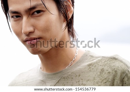 Close up beauty portrait of a young and attractive japanese asian man face getting wet under the rain and being thoughtful against a white cloudy winter sky outdoors.