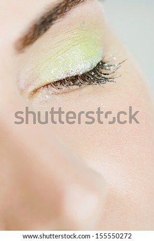 Close up beauty detail of a young and attractive woman eye wearing acidic party green glitter sparkling eyeshadow and mascara with her eyes closed, interior.