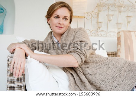 Portrait of an attractive middle aged woman laying down and relaxing on a white sofa in a neutral living room at home, being thoughtful, interior.