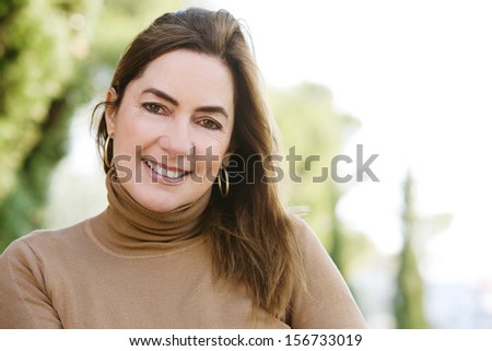 Panoramic portrait of an attractive middle aged mature woman relaxing in the countryside during a sunny autumn morning, smiling at the camera, outdoors.
