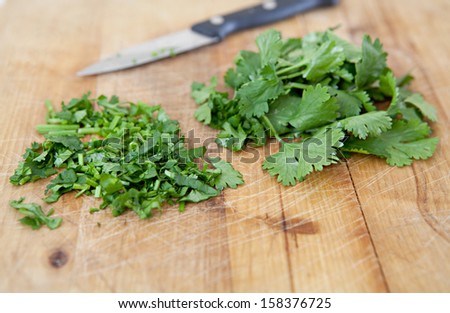 Close up detail view of a kitchen wooden chopping board with chopped green parsley aromatic herbs and a cutting knife on the side, interior.