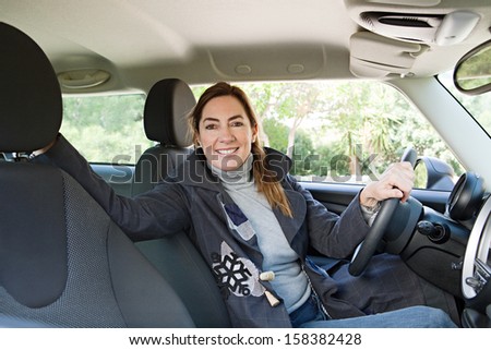 Mature woman car owner being happy and smiling in her new transport car, turning to camera and smiling during a sunny winter day while parked on a country road, car interior.