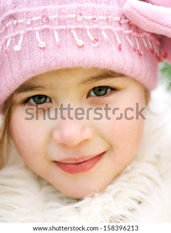 Close up beauty portrait of a young child girl wearing a winter coat, woolly hat and gloves, smiling to the camera during a cold winter day, outdoors.