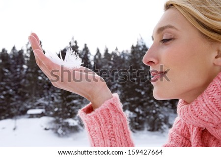 Close up profile portrait of an attractive young woman holding a light white feather in her hand while on a snow mountain landscape forest vacation during a cold winter day, outdoors.