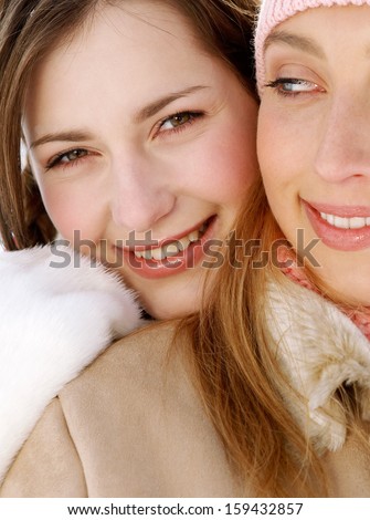 Close up of two attractive girls friends with their arms around each others shoulders, being joyful and smiling with their heads together while wearing warm coats and jackets in winter.
