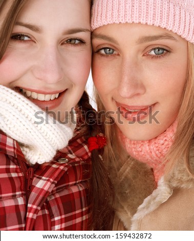 Close up of two attractive girls friends with their arms around each others shoulders, being joyful and smiling with their heads together while wearing warm coats and jackets in winter.