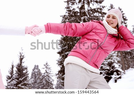 Two girls friends playing games holding their hands together and pulling in different directions, having fun during a winter day out in the snow mountains, outdoors.