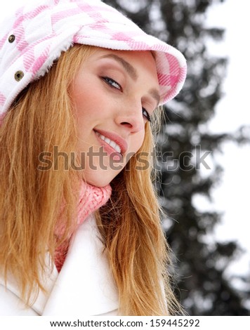 Close up side portrait of a beauty young blond woman wearing fashionable clothes and a hat, smiling while visiting the snowed mountains and trees, outdoors with nature.