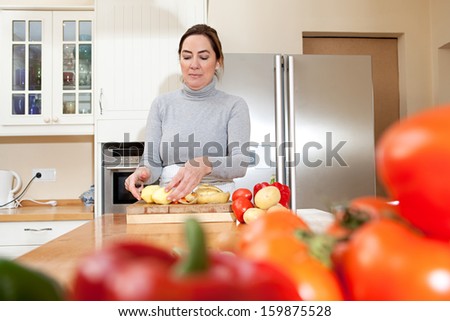 Portrait of an attractive mature woman peeling potatoes in the kitchen at home while cooking healthy organic vegetables, focused and enjoying preparing food indoors.