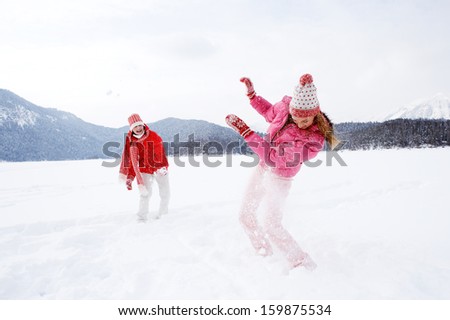Two joyful and energetic friends playing games and having fun, having a snow ball fight in the snow mountains landscape during a skiing holiday on a sunny winter day, outdoors.