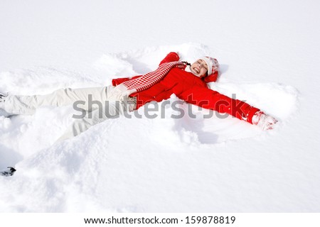 Side view of a beautiful young woman laying down on a frozen snow lake moving her arms and legs up and down creating an angel figure shape, playing games during a sunny winter  vacation.