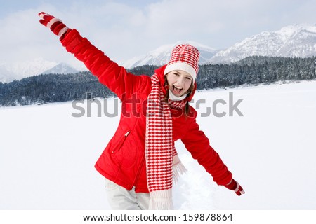 Portrait of an attractive young woman on vacation in the snow mountains, laughing and having fun, playing with her arms outstretched and running on a frozen lake during a winter day,