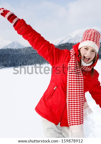 Portrait of an attractive young woman on vacation in the snow mountains, laughing and having fun, playing with her arms outstretched and running on a frozen lake during a winter day,