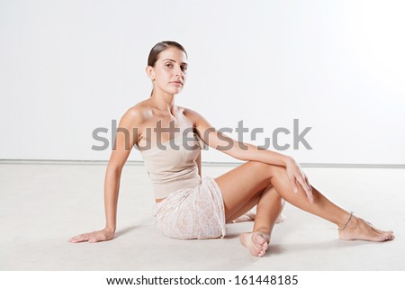 Beauty hispanic young woman sitting on a white floor with bare legs and shoulders and a dark tanned and hydrated perfect skin, and a feminine body figure and shape, interior.