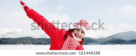 Panoramic portrait of an attractive young woman on vacation in the snow mountains, laughing and having fun with her arms outstretched and running on a frozen lake during a winter day.