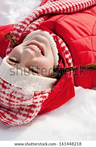 Over head view of a young woman laying down on a frozen snow lake moving her arms up and down creating an angel figure shape, playing games while on vacation during a sunny winter day.