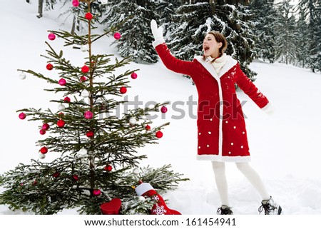Side view of an attractive girl celebrating Christmas and decorating a natural Xmas tree with bar balls while on holiday in the skiing snow mountains during a cold winter day outdoors.