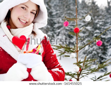 Close up portrait of an attractive girl with a natural Christmas tree with bar balls, holding a stocking full of candy sweets and joyfully smiling in the snow mountains outdoors.