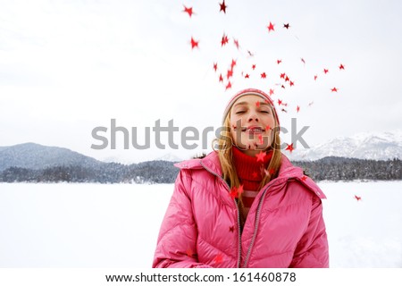 Portrait of an imaginative, young and beautiful woman in the snow mountains landscape throwing star shaped glitter up in the sky during a cold Christmas winter day outdoors in nature.