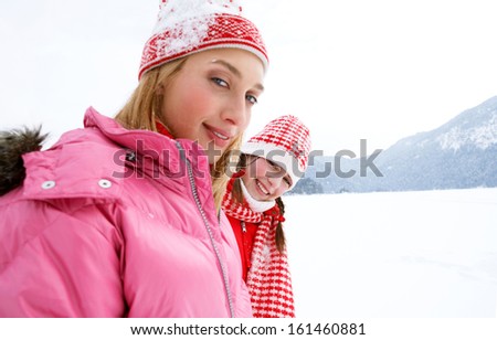 Side portrait view of two young and attractive women enjoying a skiing vacation together, smiling in the snow mountains landscape and turning to smile at the camera during a winter day.