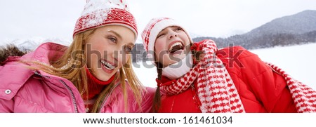 Portrait view of two joyful young women friends having fun and laughing while skiing in a white snow landscape scenery in the mountains, laughing with big expressions, outdoors.