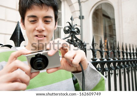 Young Japanese man using a photographic digital camera to take pictures while on holiday in the city of London, sightseeing and enjoying a city break trip, outdoors.
