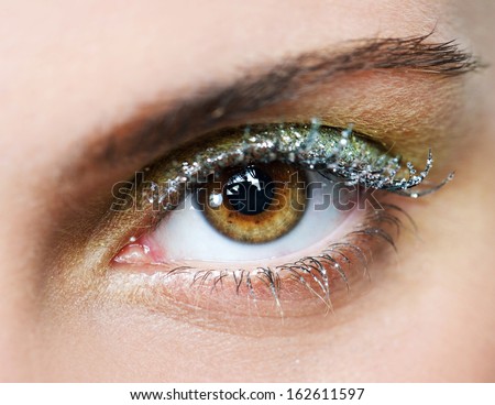 Close up beauty view of an attractive young woman eye looking into the camera, wearing fantasy party green and yellow eye shadow make up and glitter mascara.
