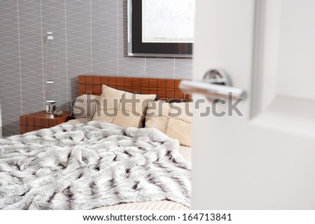 Still life view through an open door of a luxury bedroom with a wooden bed frame and a picture on the wall, showing graphic masculine wallpaper and a fake fur blanket. Interior with no people.