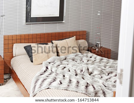 Still life view through an open door of a luxury bedroom with a wooden bed frame and a picture on the wall, showing graphic masculine wallpaper and a fake fur blanket. Interior with no people.