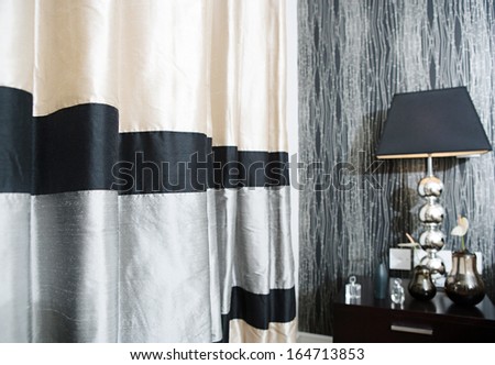 Still life view of a stylish and luxury hotel bedroom with a bedside lamp, soft silk fabric curtains and a graphic masculine wallpaper. Home interior with no people.