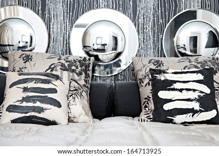 Close up view of a designer hotel bedhead decorated with round mirrors and silk pillows and cushions against an organic texture wall in a luxurious and elegant bedroom. Home interior with no people.
