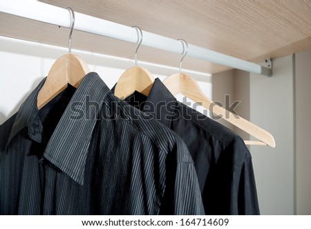 Still life of a professional hotel room wardrobe with a business man tidy black shirts hanging from wooden hangers. Home interior detail with no people.